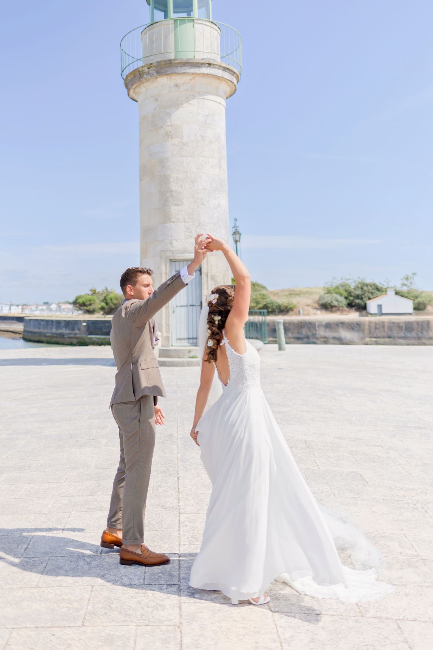 Couple dances playfully in front of white lighthouse on their wedding day.