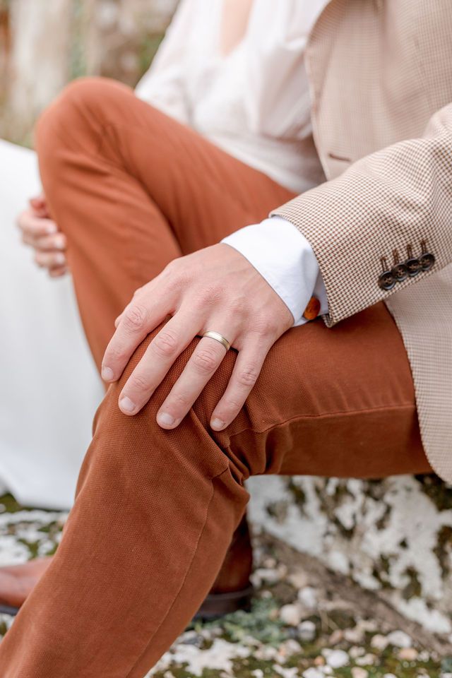 Close-up of wedding ring detail with beige suit jacket and rust-colored pants.