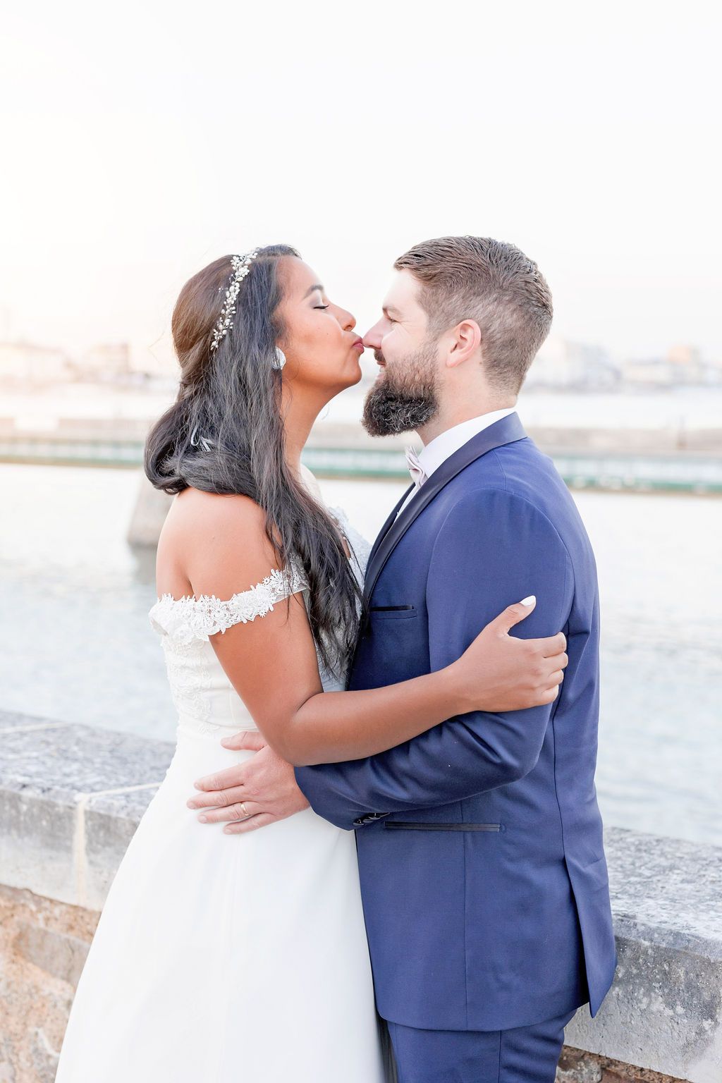 Loving couple shares a kiss during their wedding photoshoot on a coastal bridge.