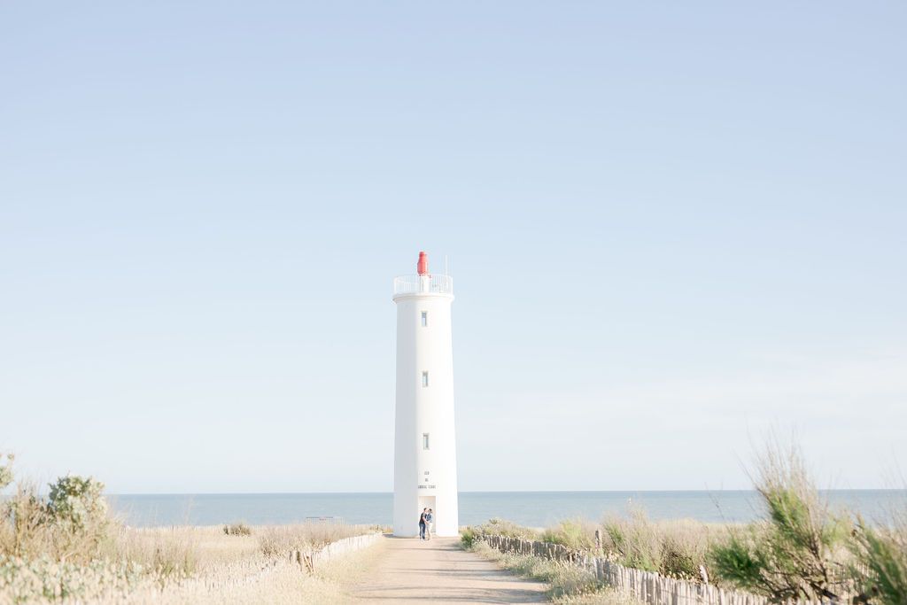 Scenic view of white lighthouse on beach with ocean horizon in background.