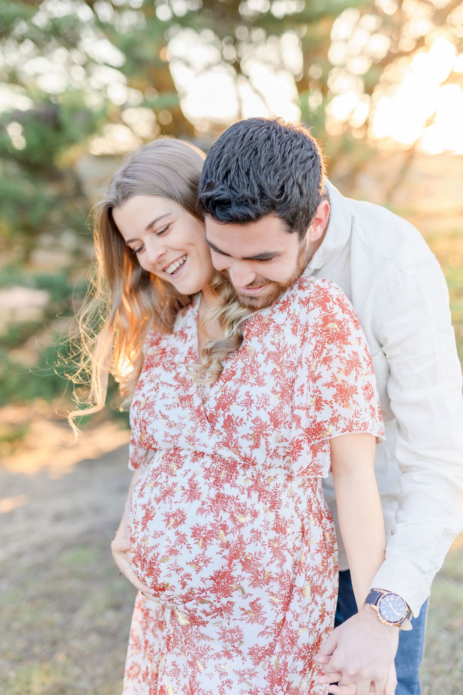 A couple sharing a tender moment together at sunset, with her wearing a floral dress.