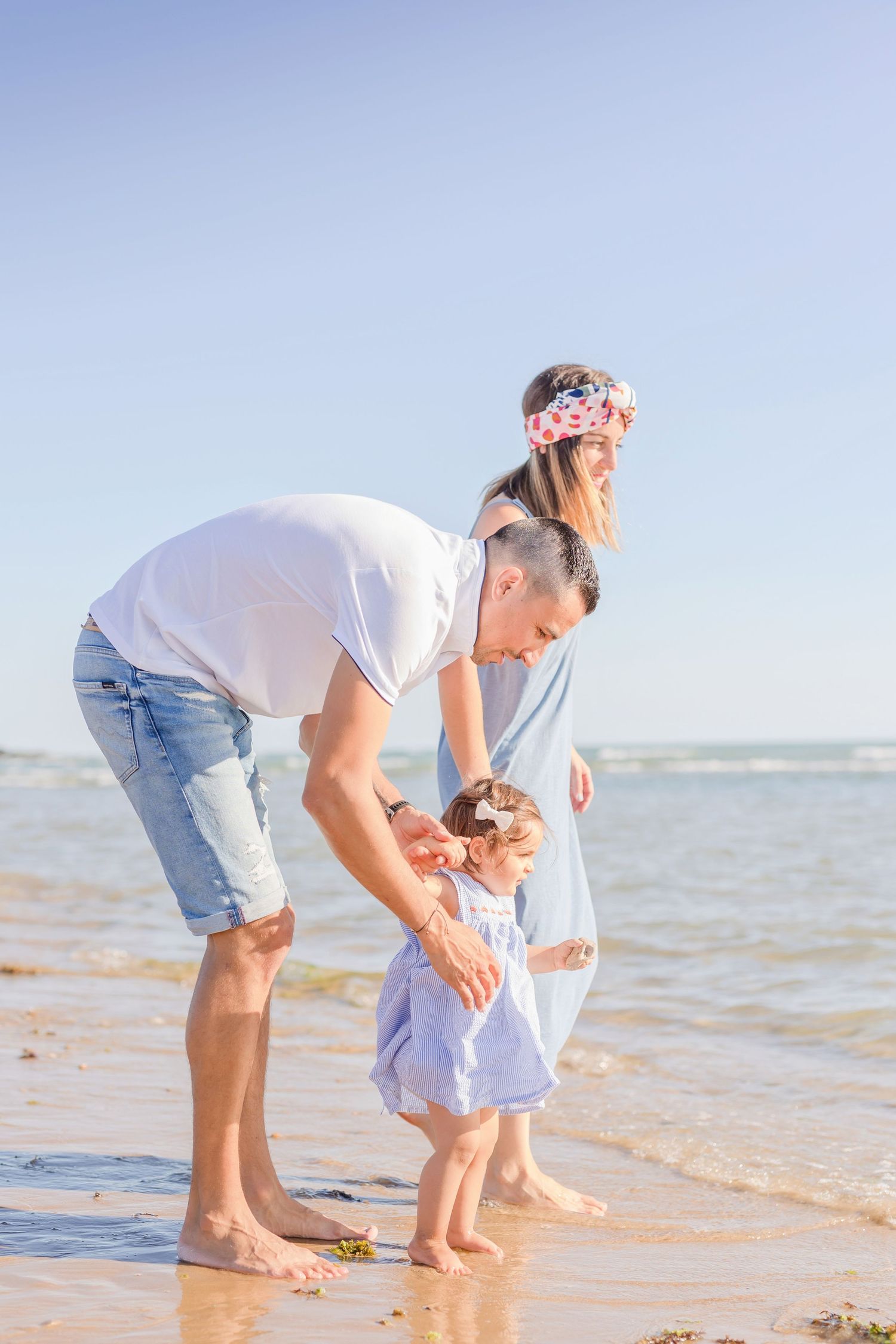 Family playing together in shallow ocean water on a sunny beach day.
