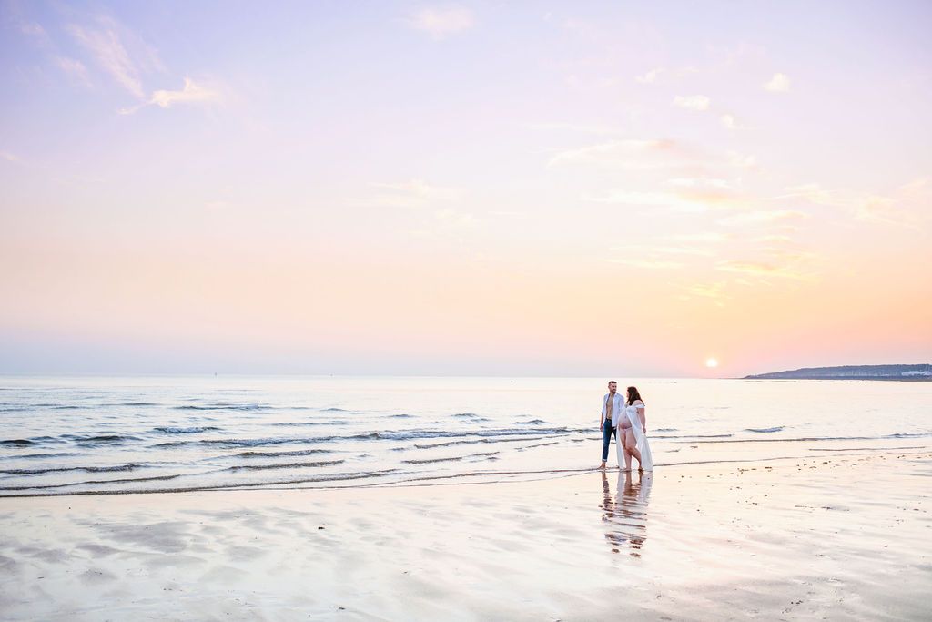 Silhouettes of two people standing on a beach at sunset with waves reflecting light.