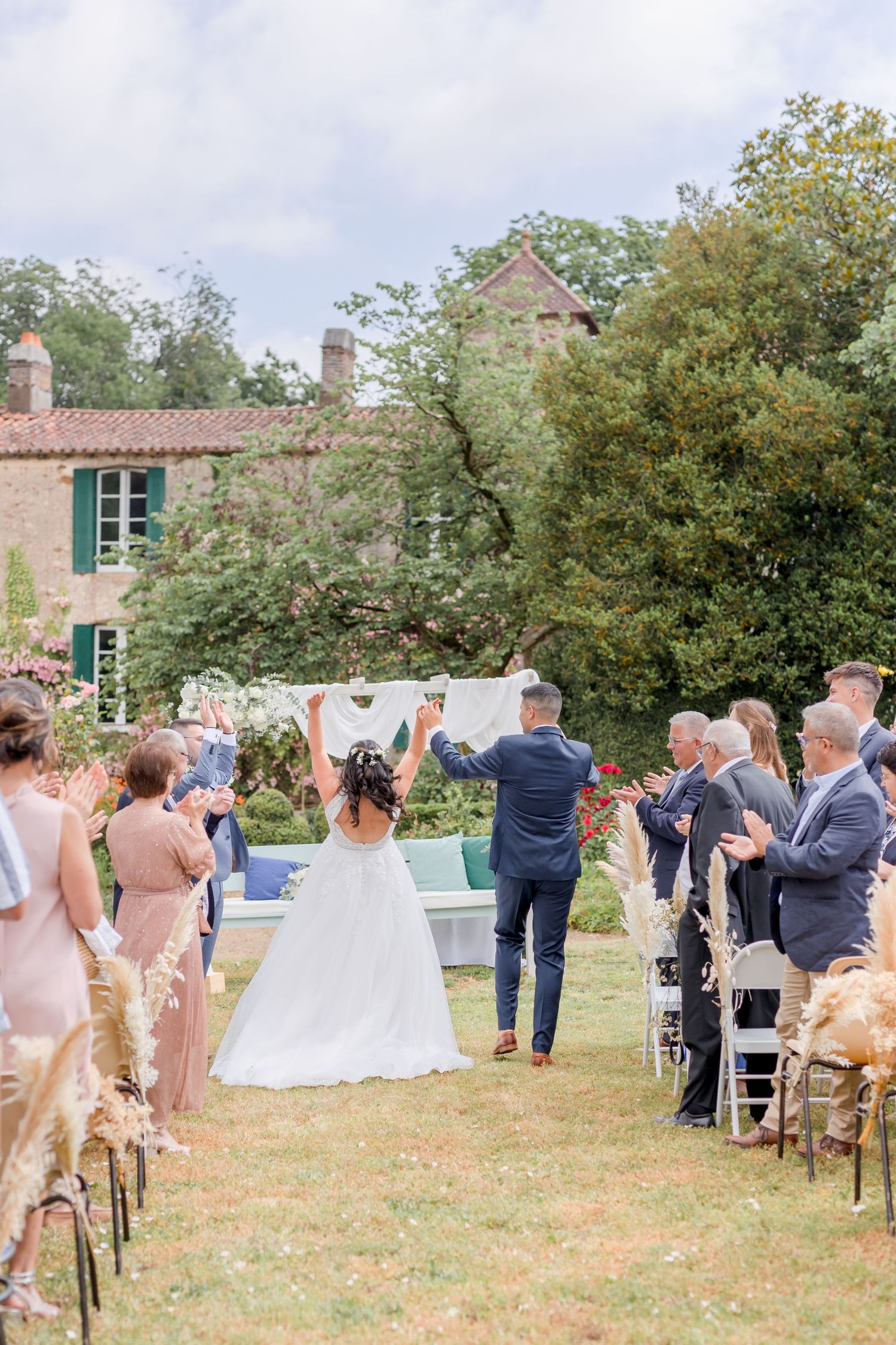 Outdoor wedding ceremony setup with vintage brick building backdrop and white chairs.