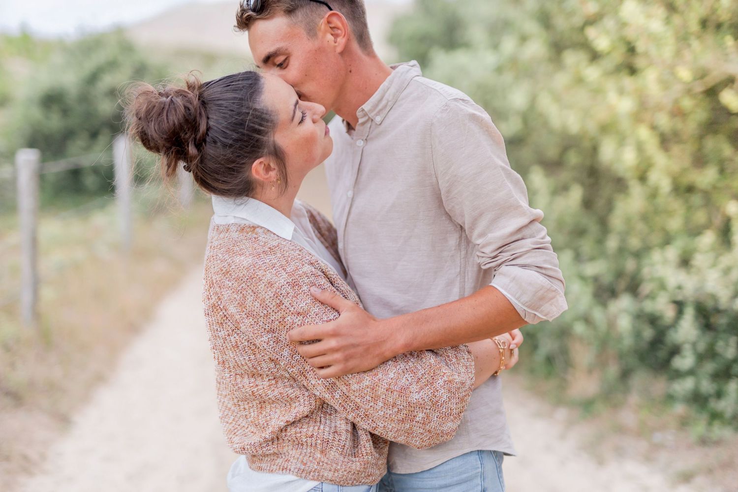 Romantic couple embracing on pathway with natural scenery behind them.