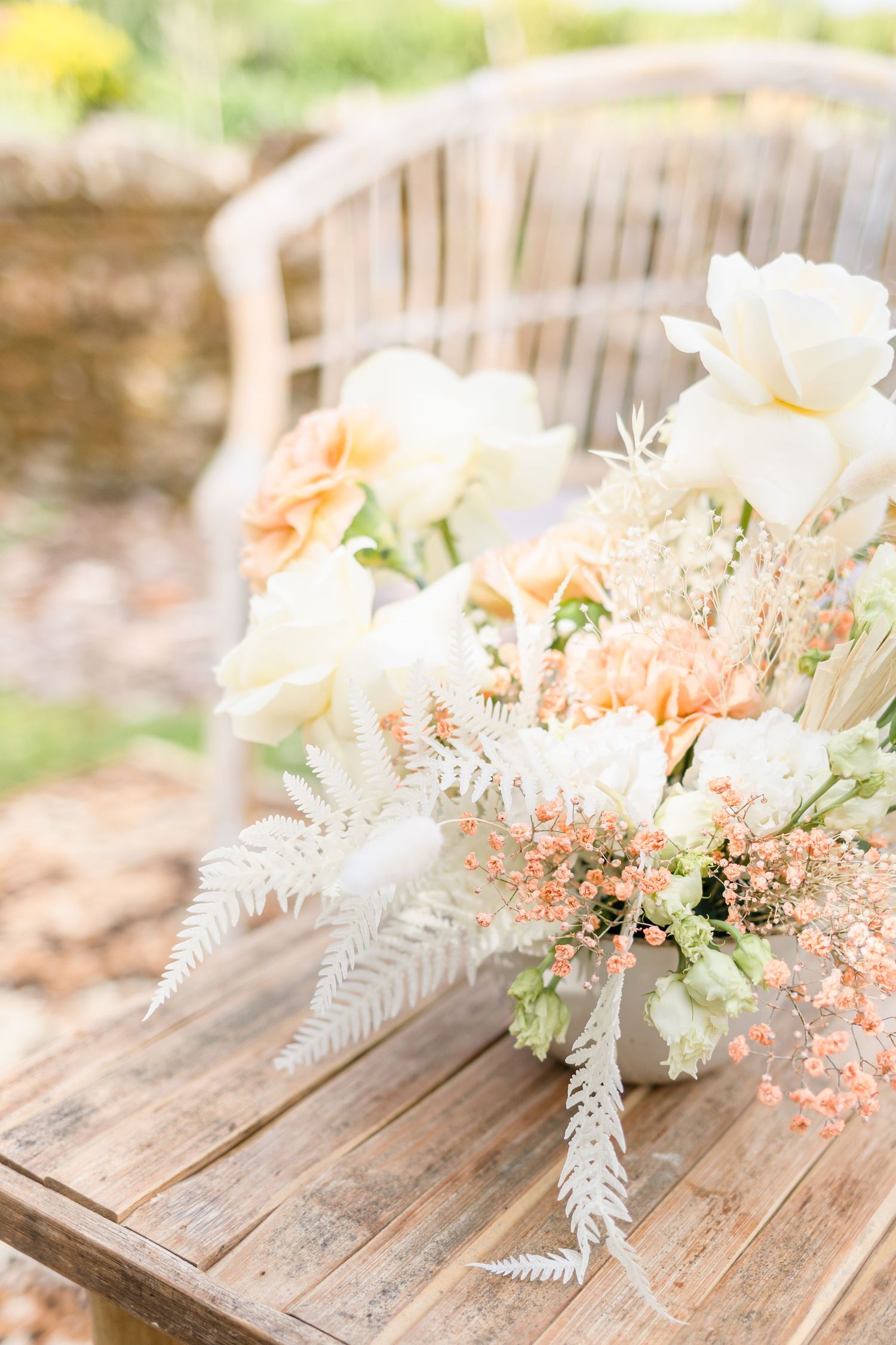 Elegant white and peach floral centerpiece with ferns on a rustic wooden table.