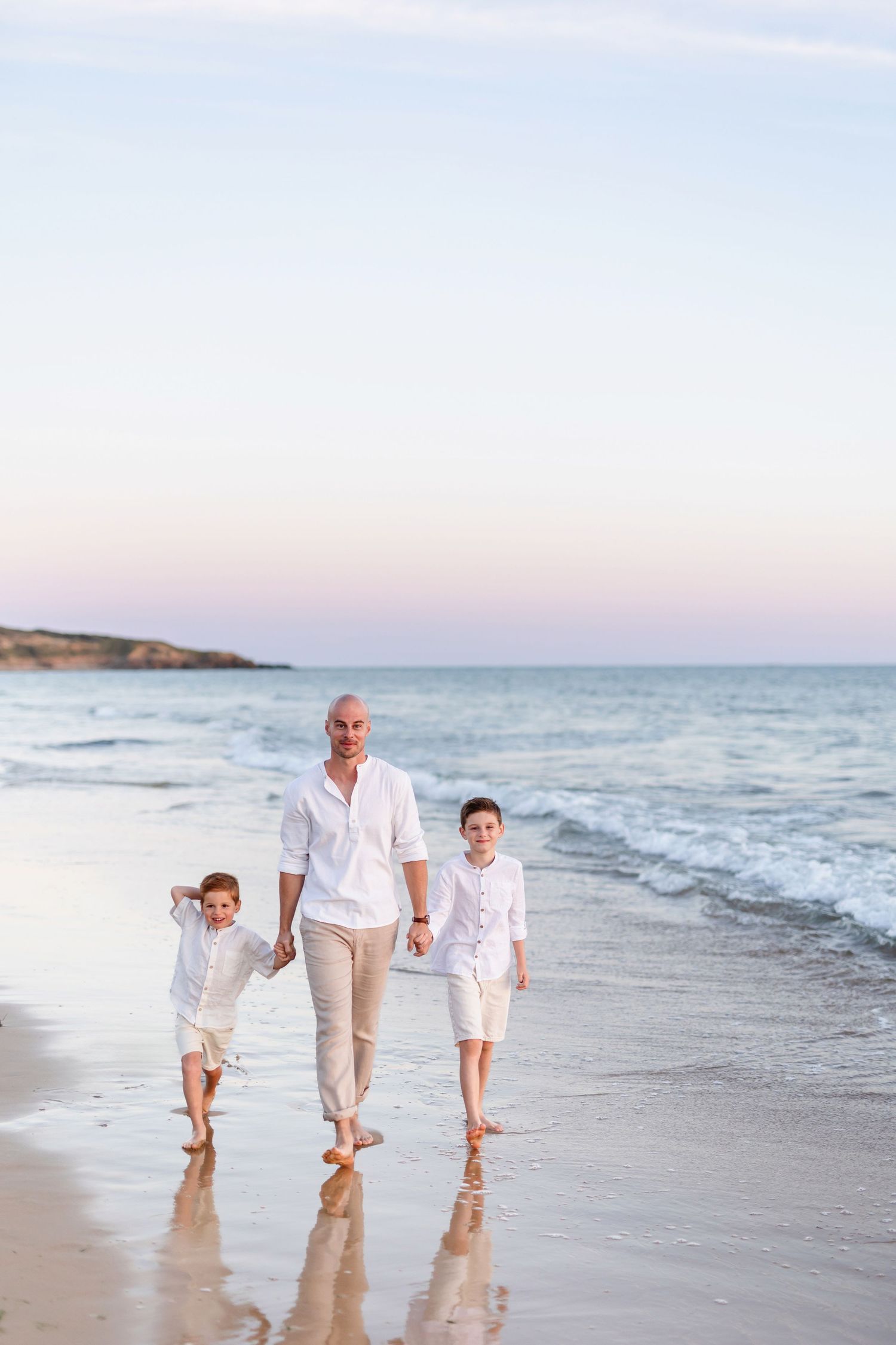 Family walking together along the water's edge on a peaceful beach at sunset.