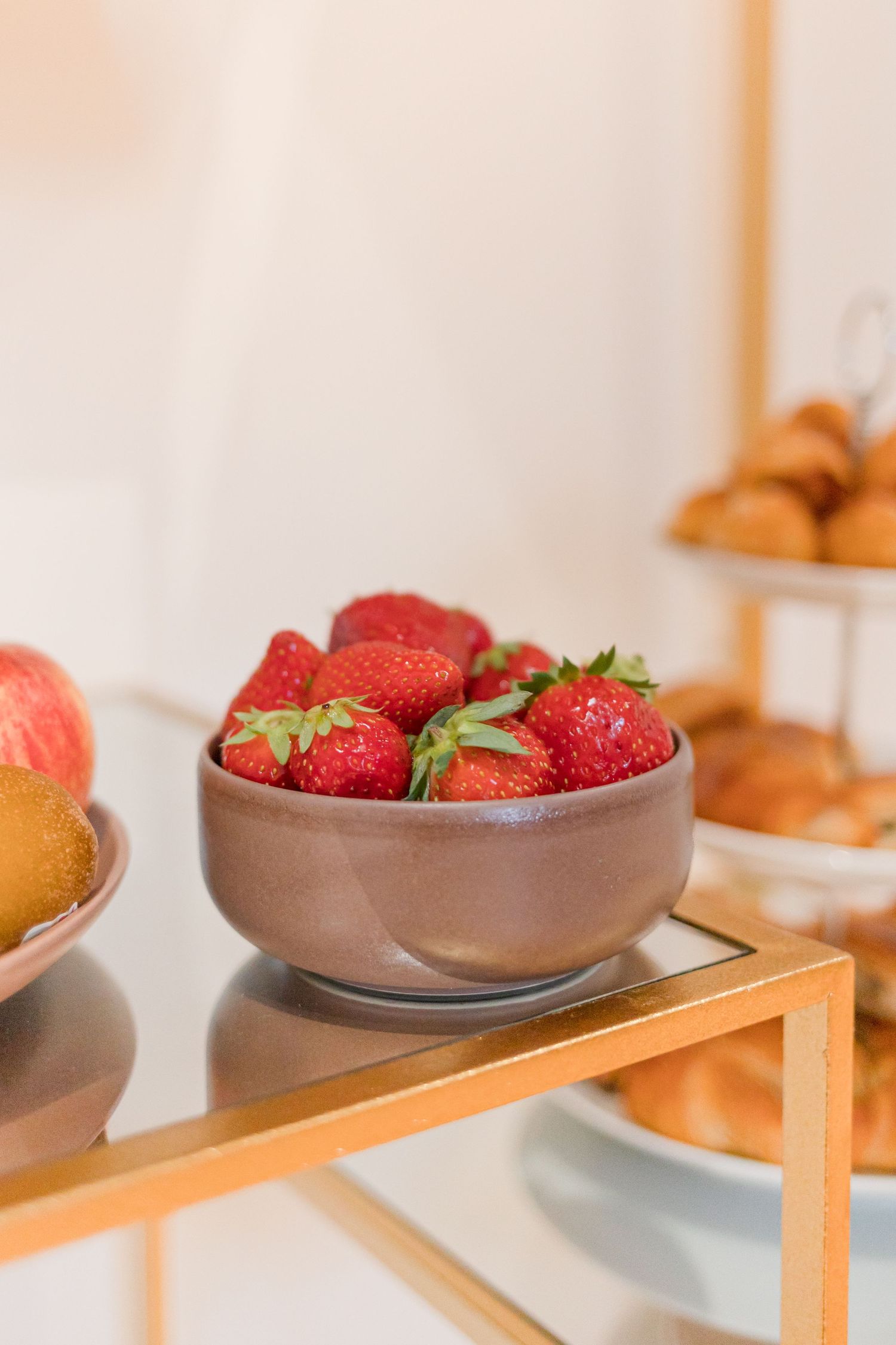 Fresh red strawberries displayed in a brown ceramic bowl on a wooden shelf.