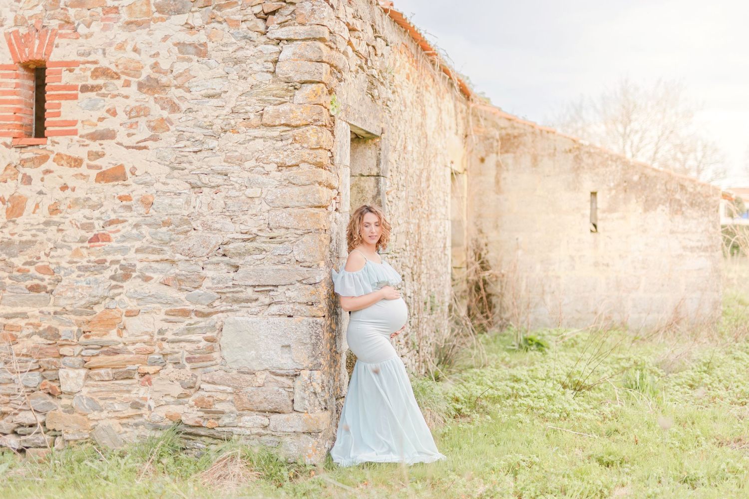 Maternity portrait by old stone building in soft sunlight.