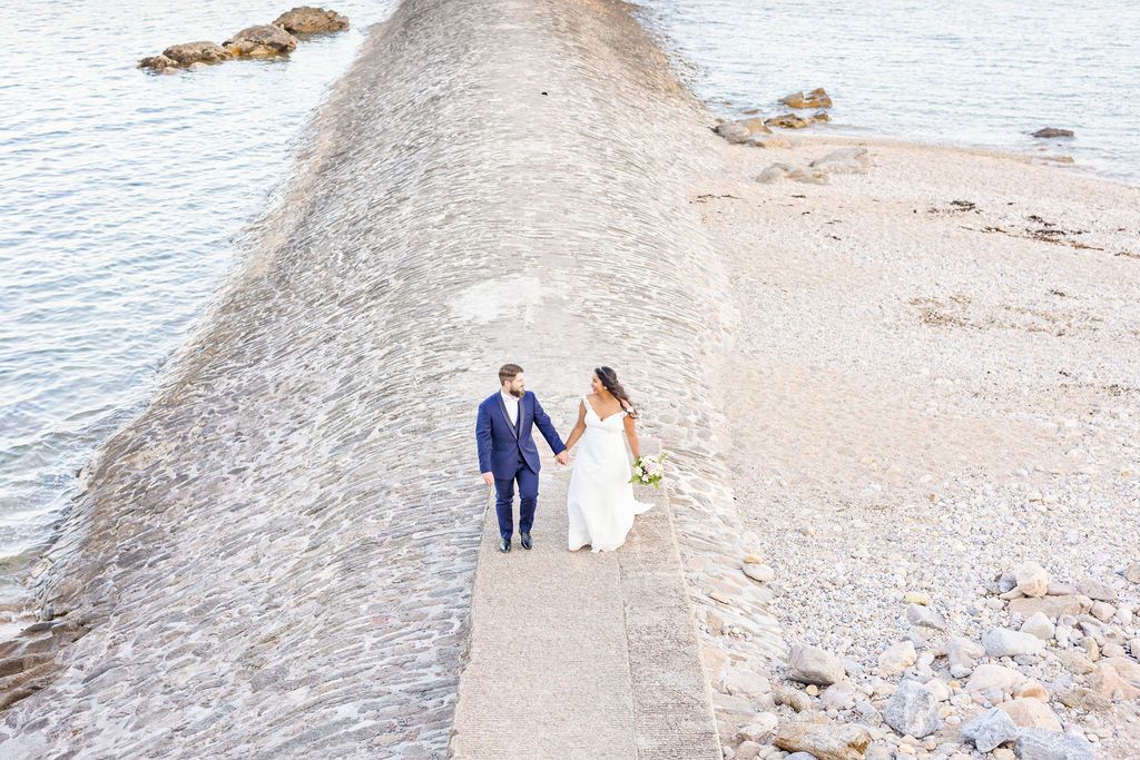 Wide beach landscape with wedding couple walking along rocky shoreline.