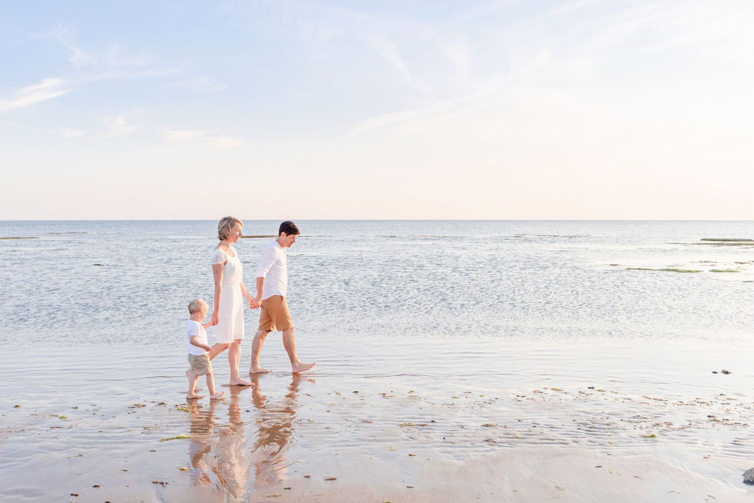 People walking together on a serene beach at sunset with footprints in the wet sand.