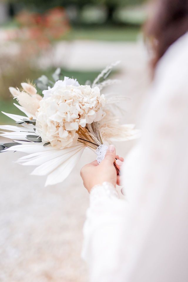 Hands holding a romantic dried floral bouquet in soft peachy white tones.