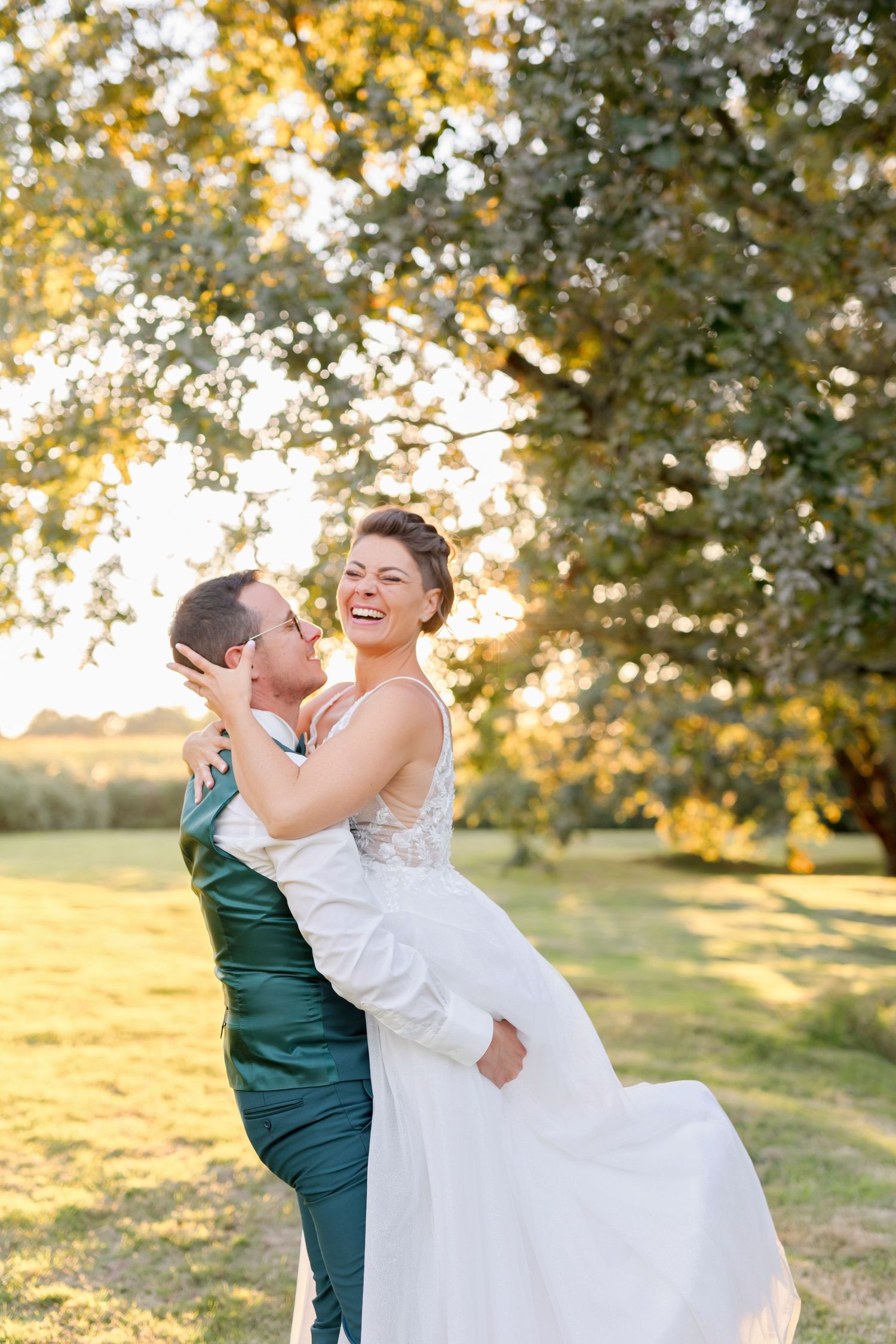 Joyful wedding moment captured as couple share a playful lift pose in sunlit outdoor setting.