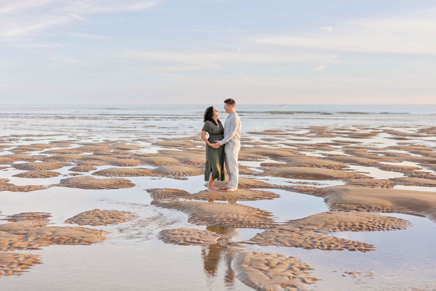 Two people stand together on textured sand formations during low tide at the beach.