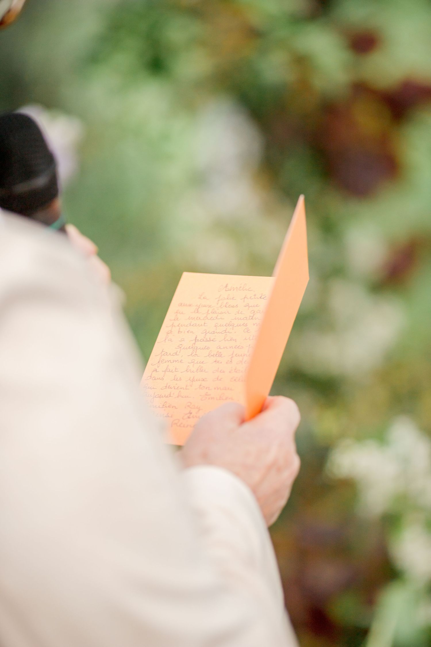 Close-up of hands holding orange ceremony program outdoors.