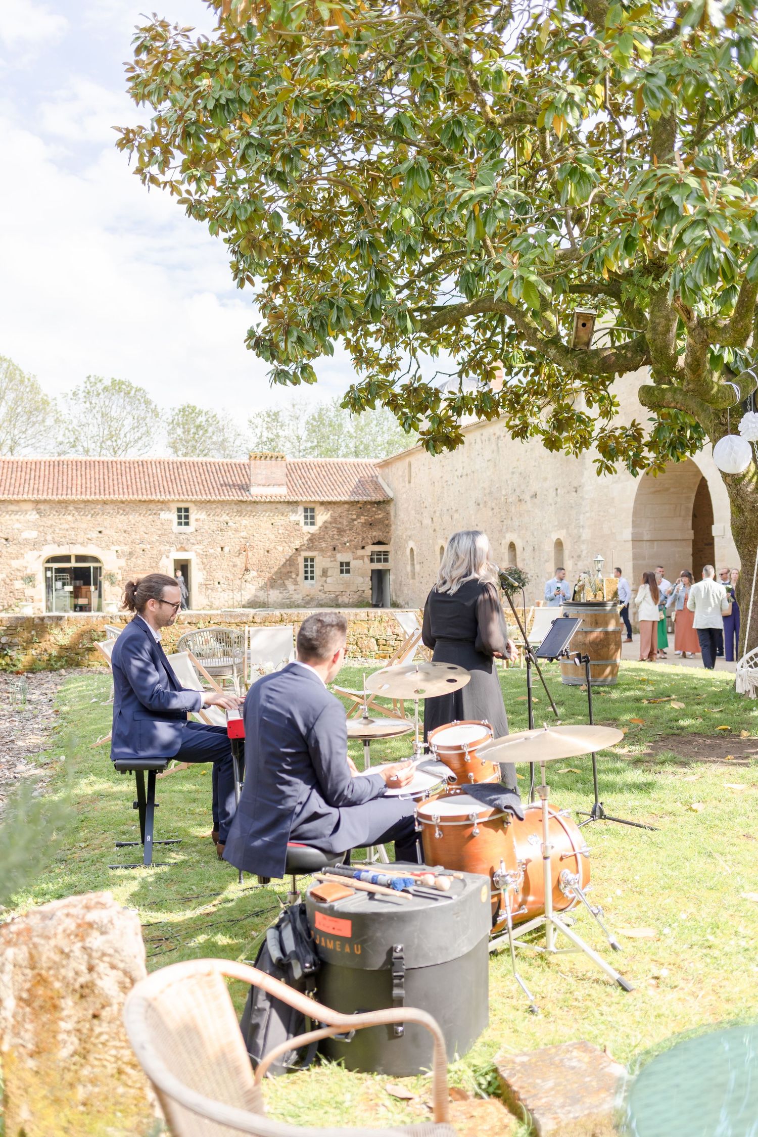 Musicians performing outdoors with drums and instruments under a large tree.