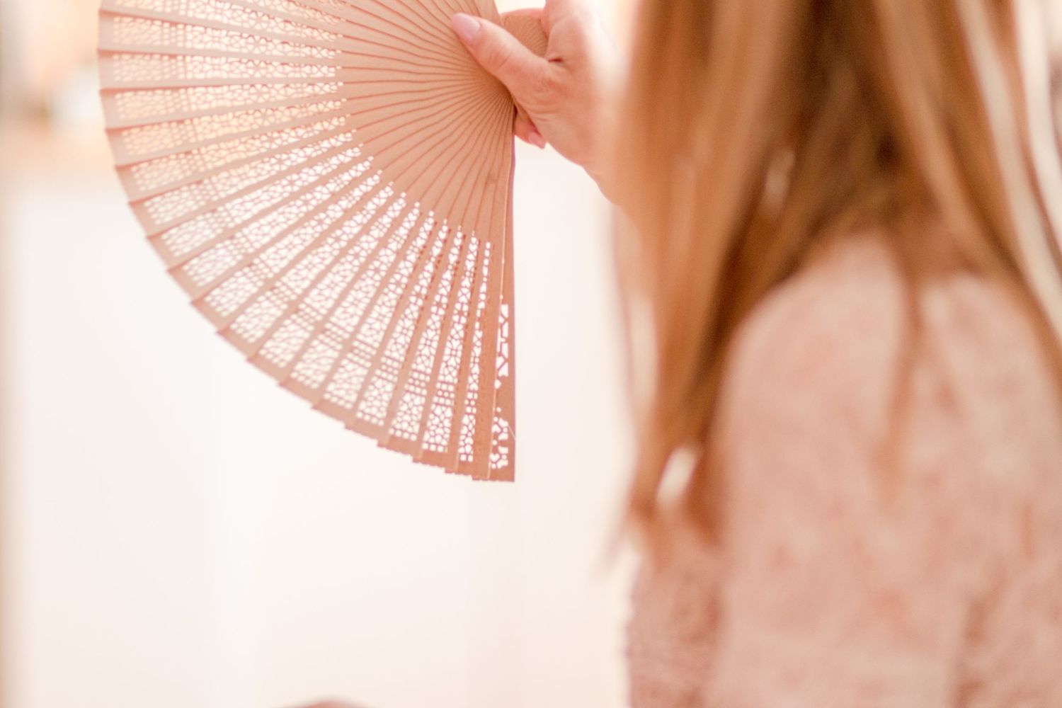 Pink paper fan held against blurred bright background creating an elegant aesthetic.