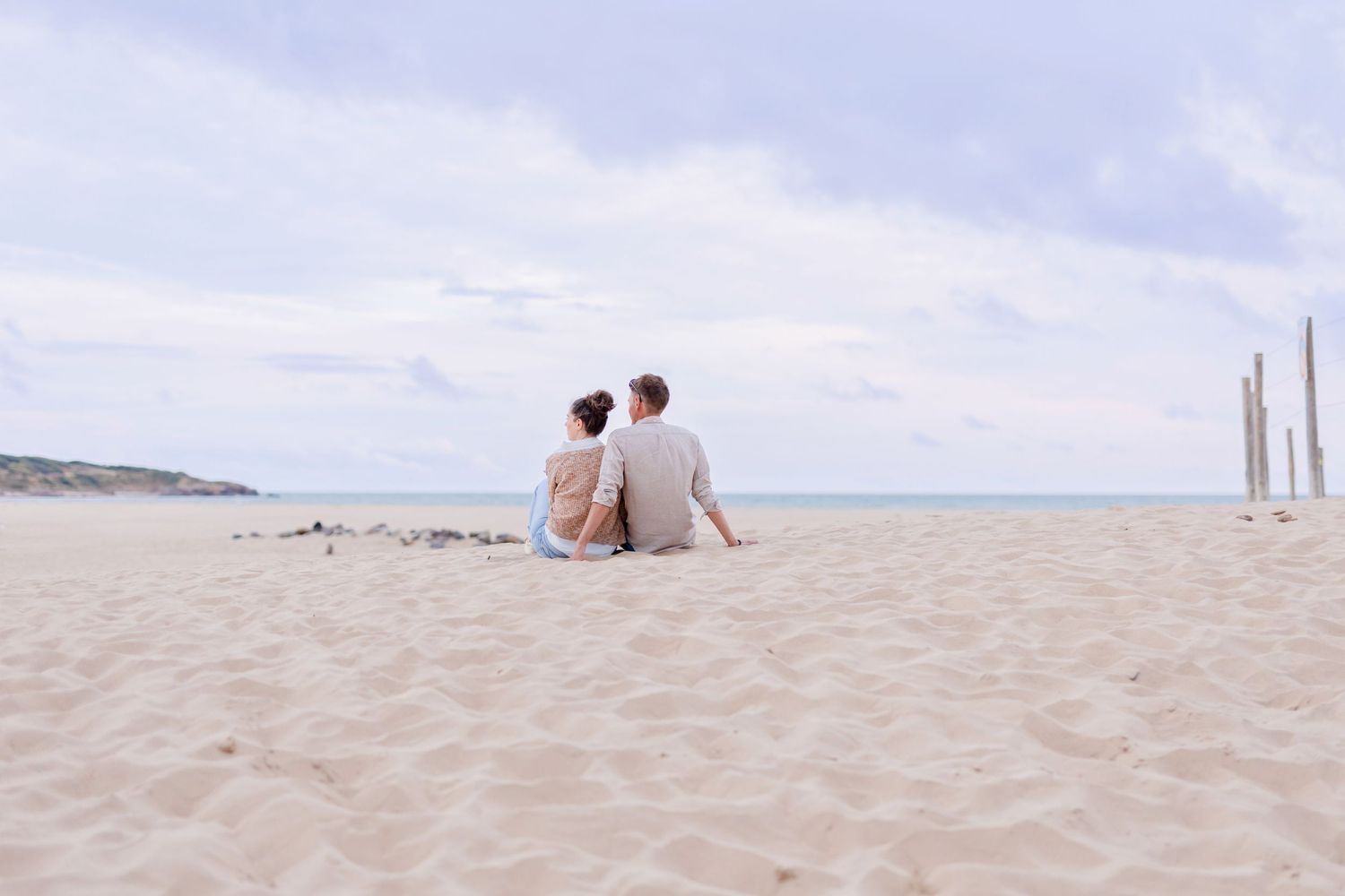 Couple sitting together on sandy beach overlooking ocean view.