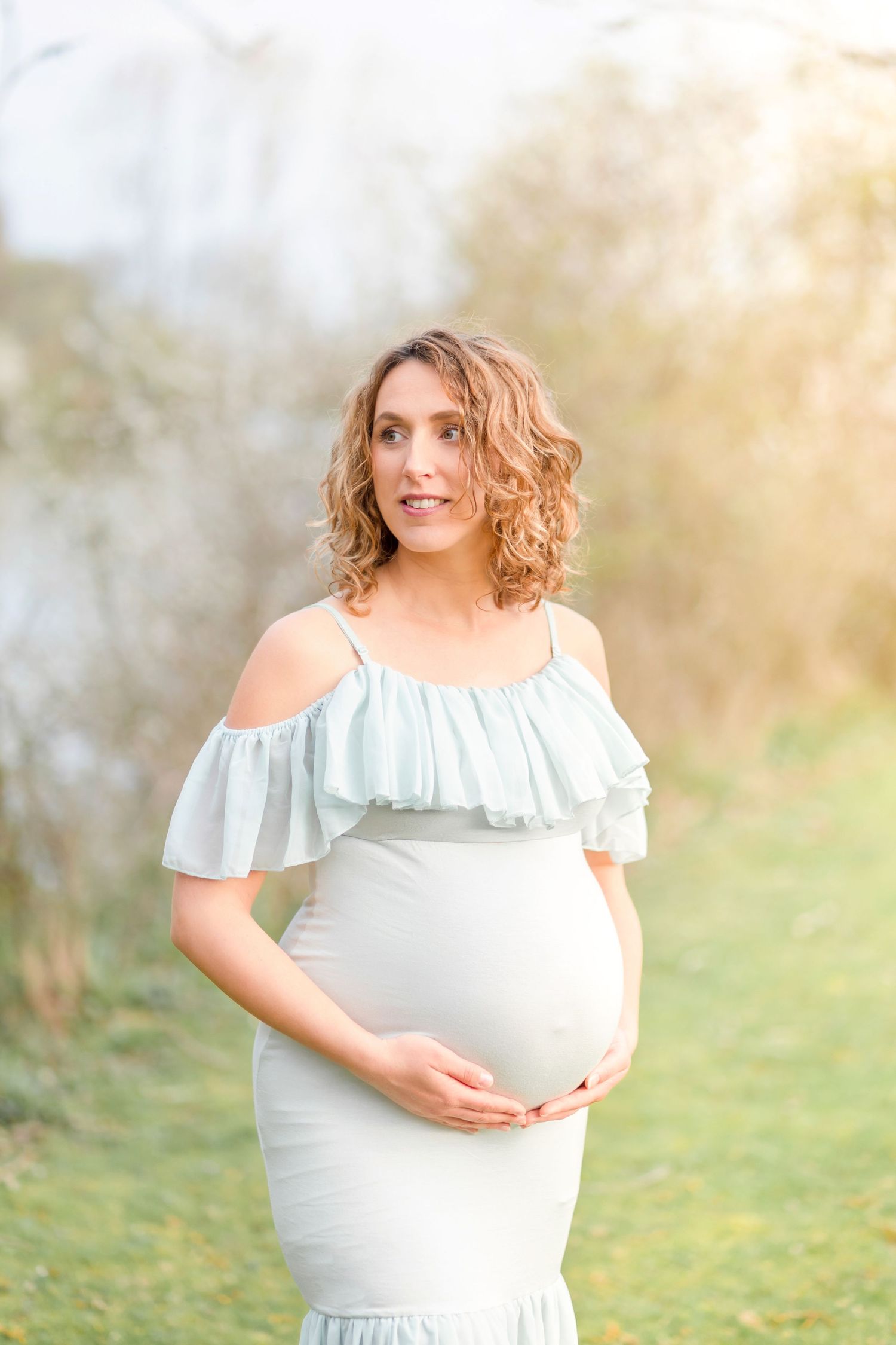 An ethereal maternity portrait featuring a flowing white gown against a soft natural background.