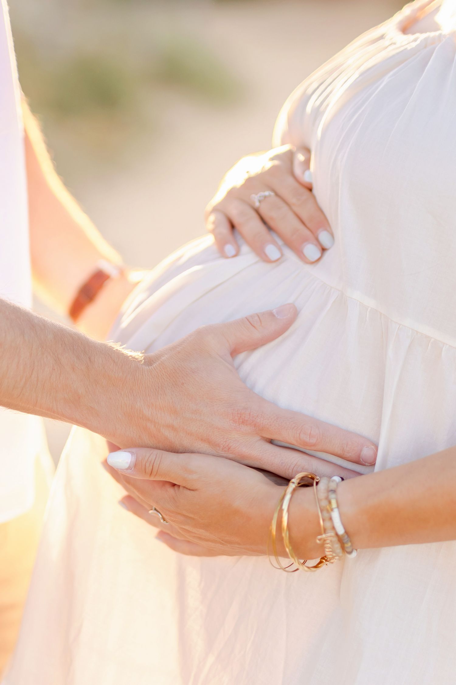 Close up of hands cradling pregnant belly during maternity photoshoot at sunset.