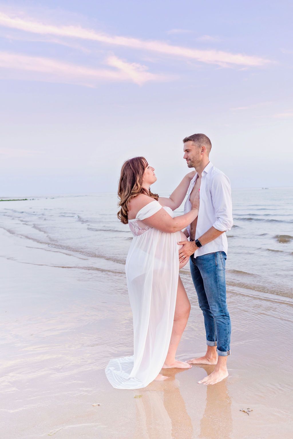 A romantic couple shares intimate moments during their beach maternity photoshoot at sunset.