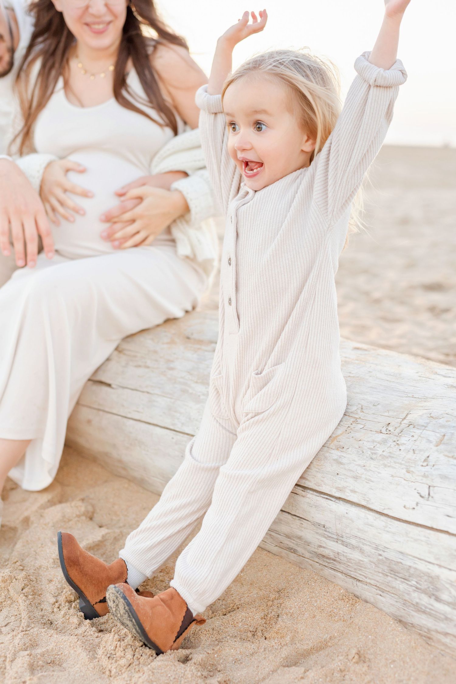 Excited child in cream outfit jumping with joy on wooden planks at the beach.