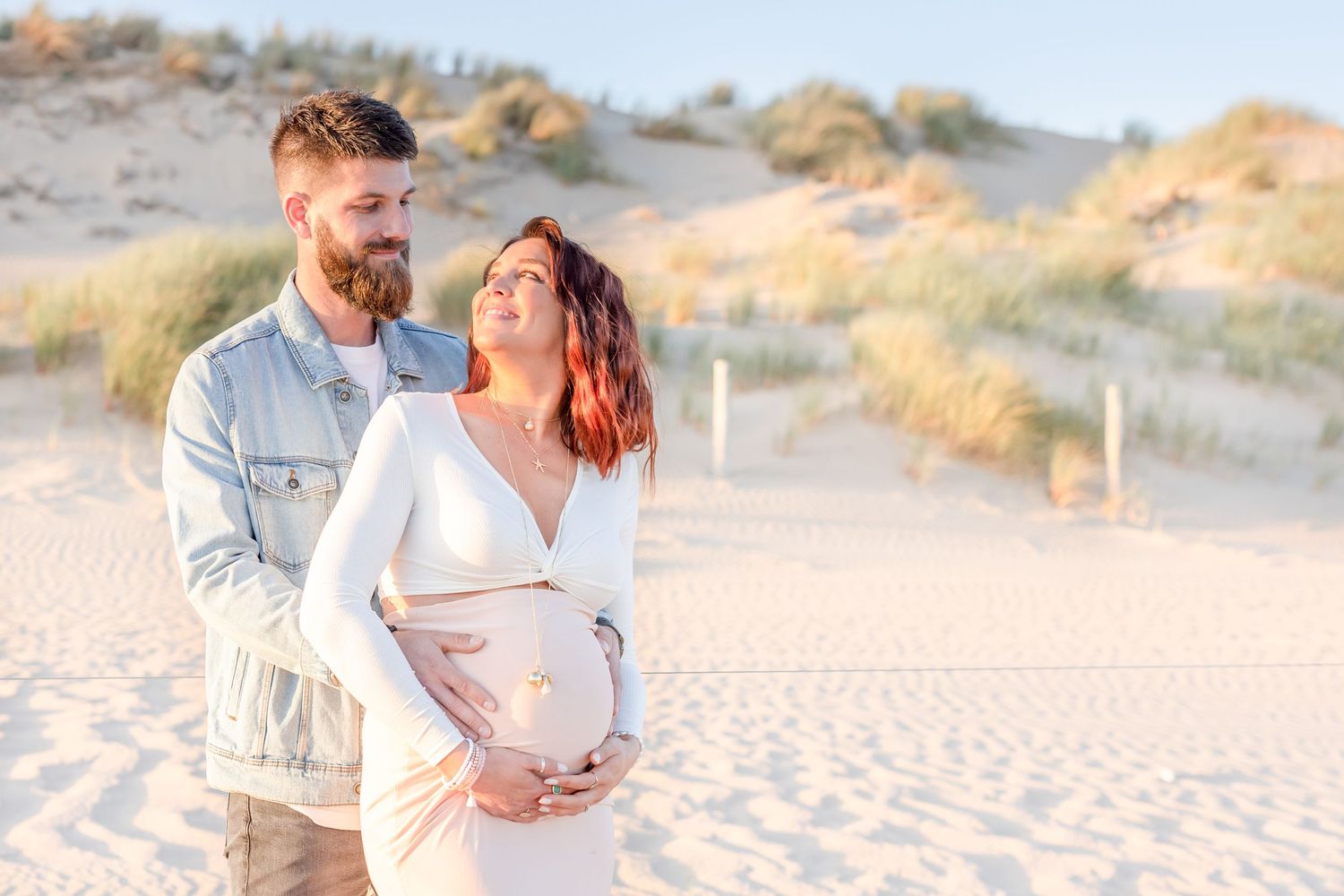 Couple shares intimate moment on beach during maternity photoshoot at golden hour.