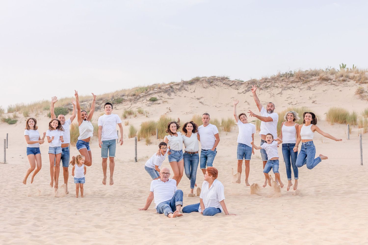 Multi-generational family group lounges on sand dunes for casual outdoor portraits.