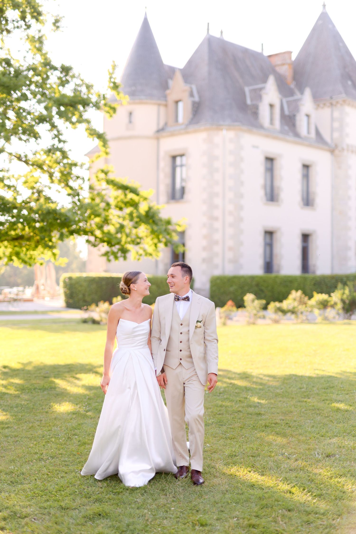 Wedding couple poses against stunning French chateau backdrop at sunset.