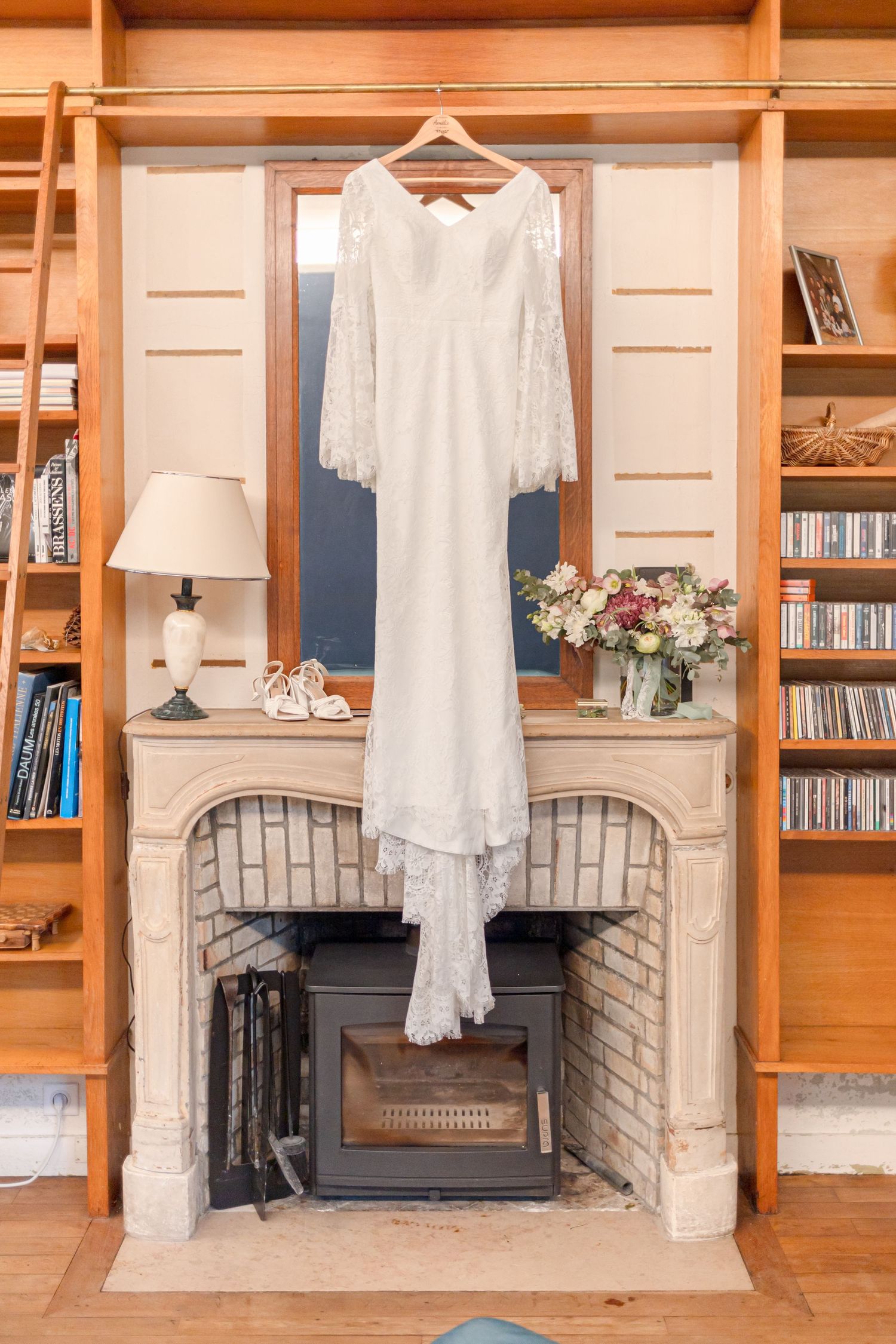 Wedding dress and accessories displayed against wooden built-in shelves with a stone fireplace.