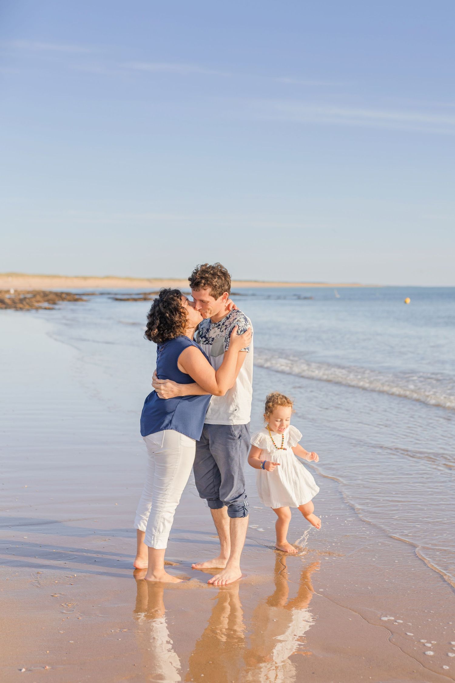A loving family moment captured on a sunny beach as they walk barefoot along the shore.
