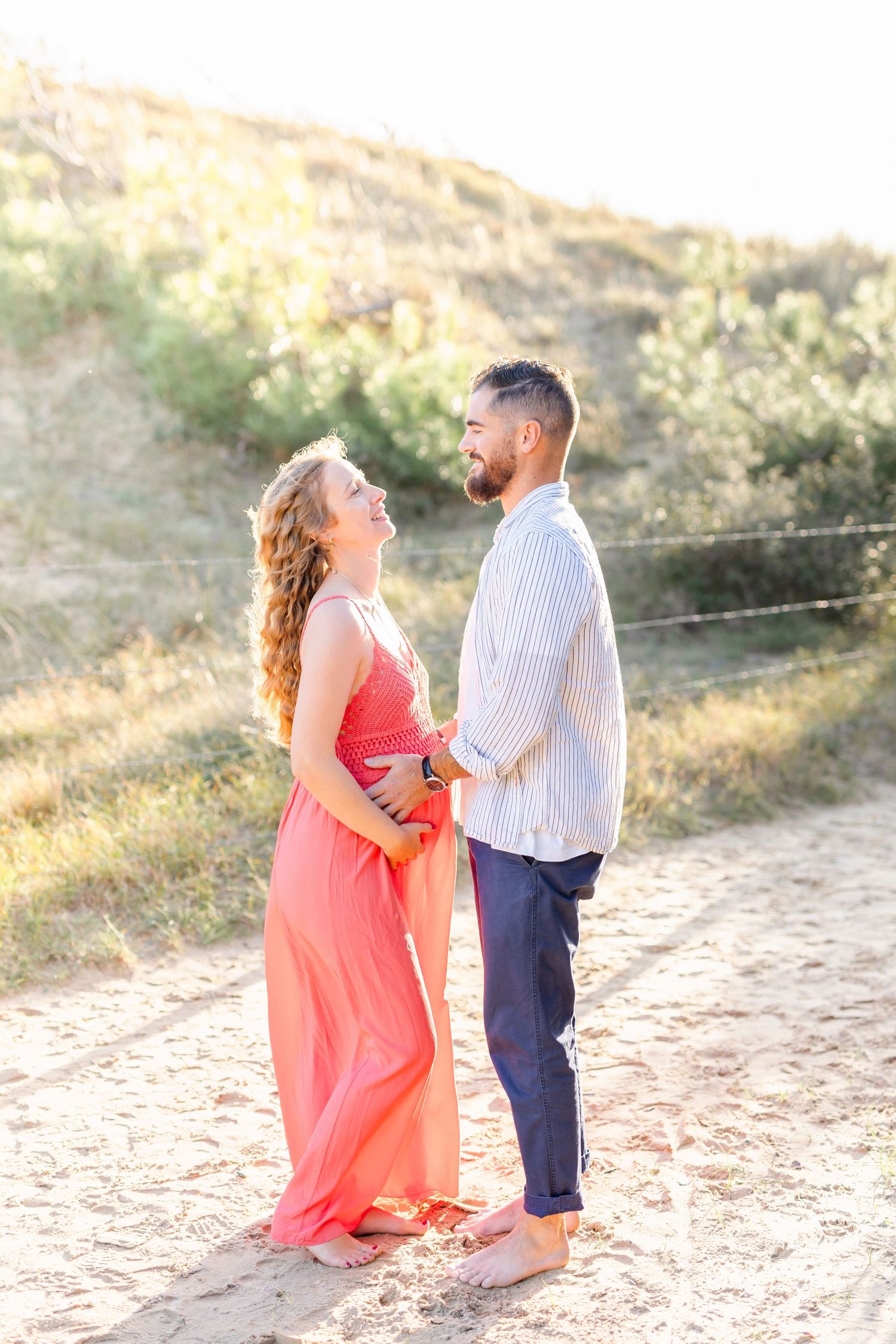 A couple shares an intimate moment on a sandy trail during golden hour.