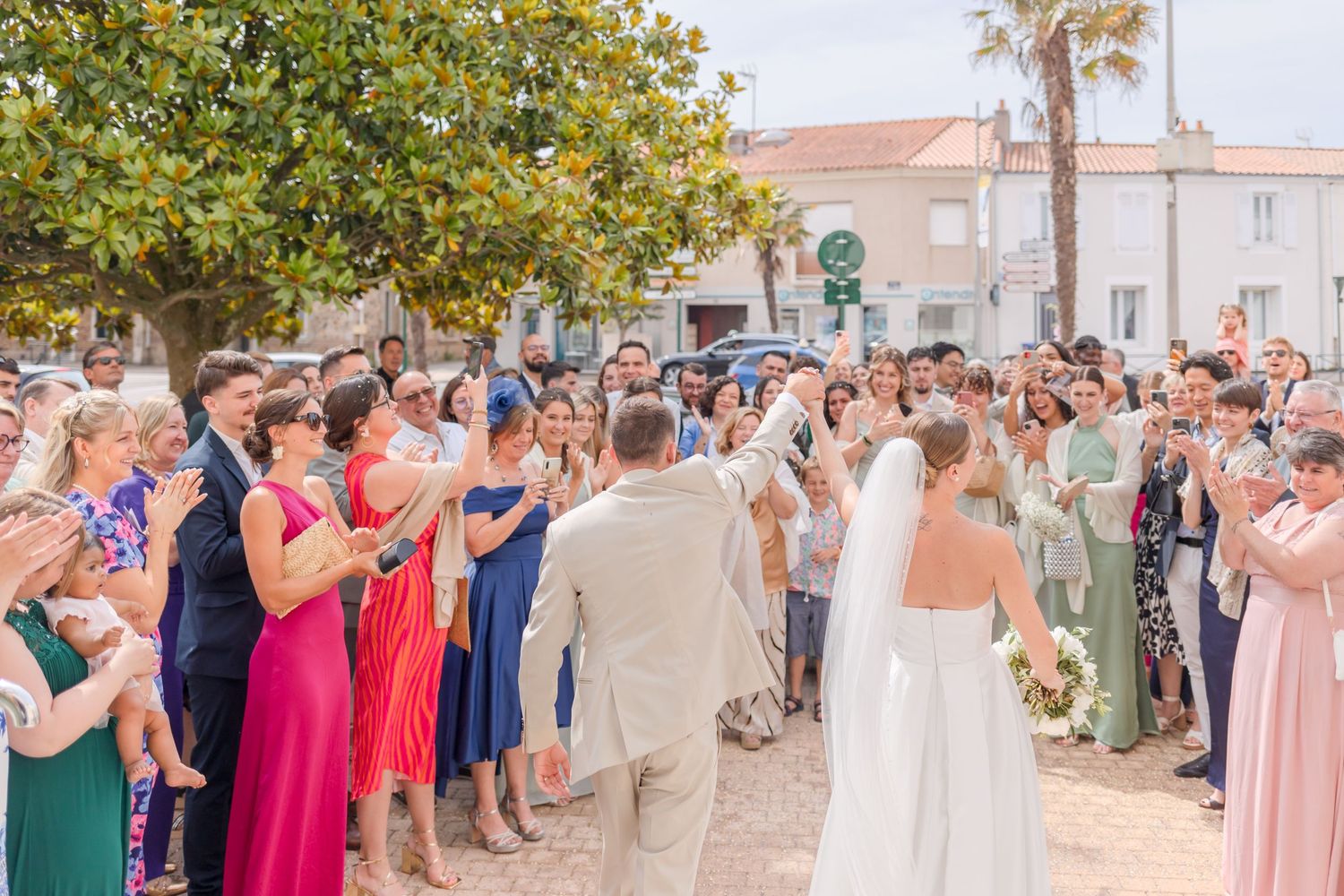 Wedding guests line up on both sides cheering and clapping for the newlyweds at an outdoor celebration.