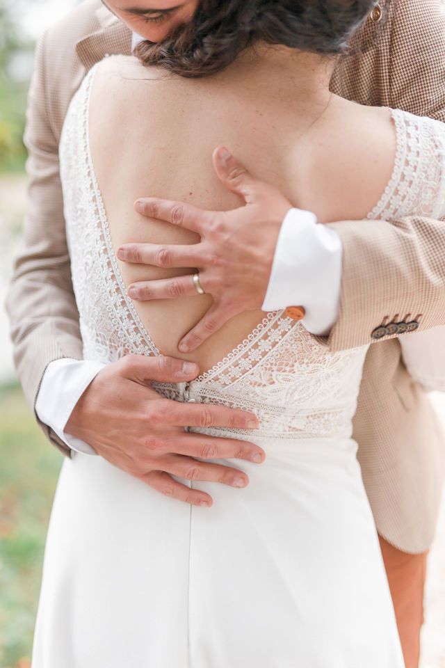 Intimate moment captured showing hands embracing waist in lace wedding dress.