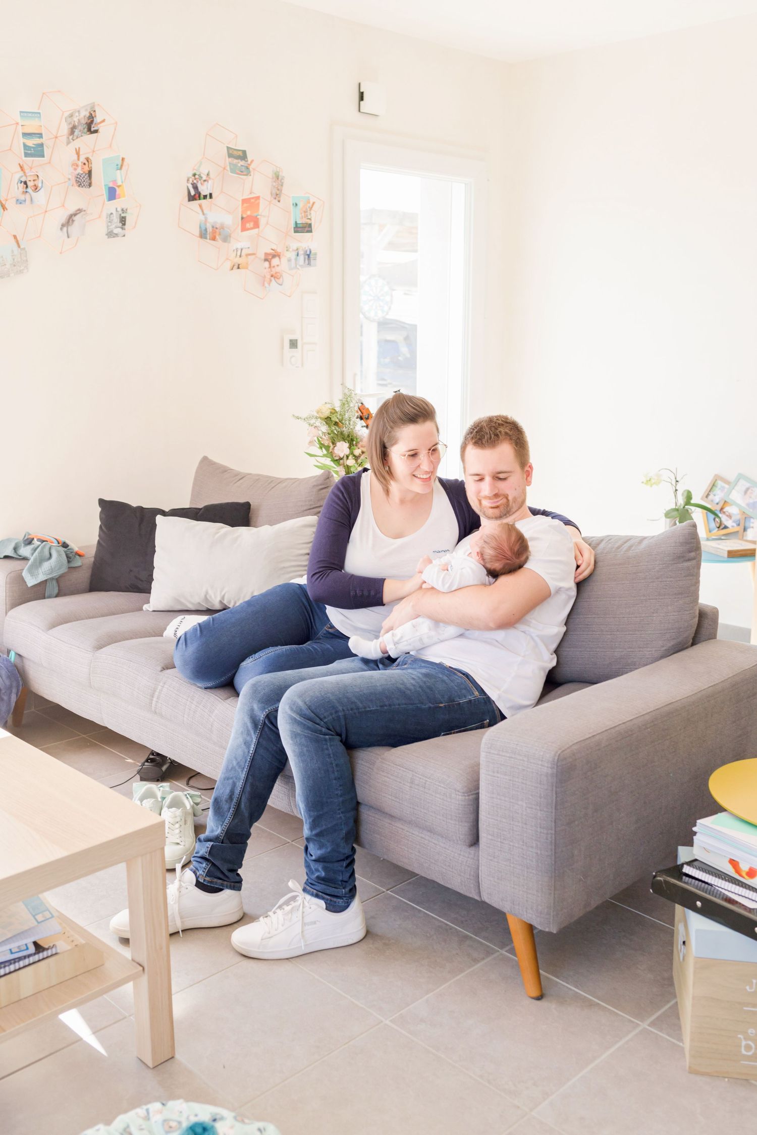 Family relaxing together on gray sectional sofa in bright living room with photos on wall.