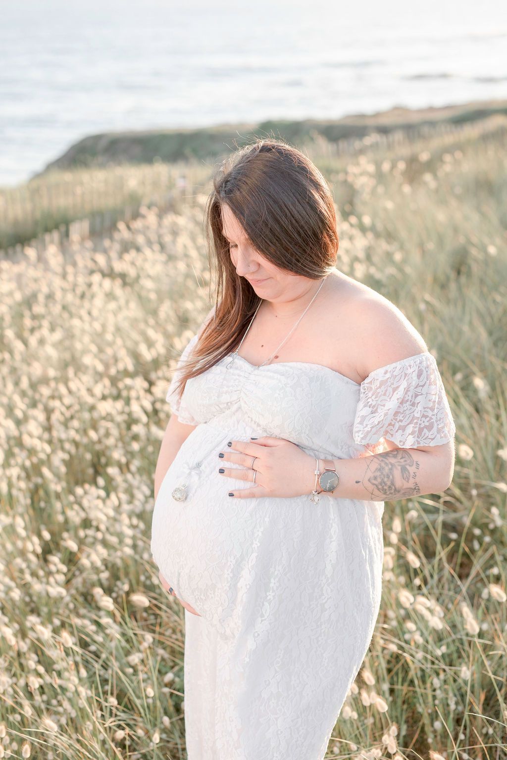Side profile maternity photo with coastal cliffs and wildflowers in background.