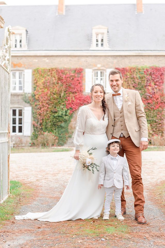 Wedding couple poses in front of a historic stone building with red autumn vines.