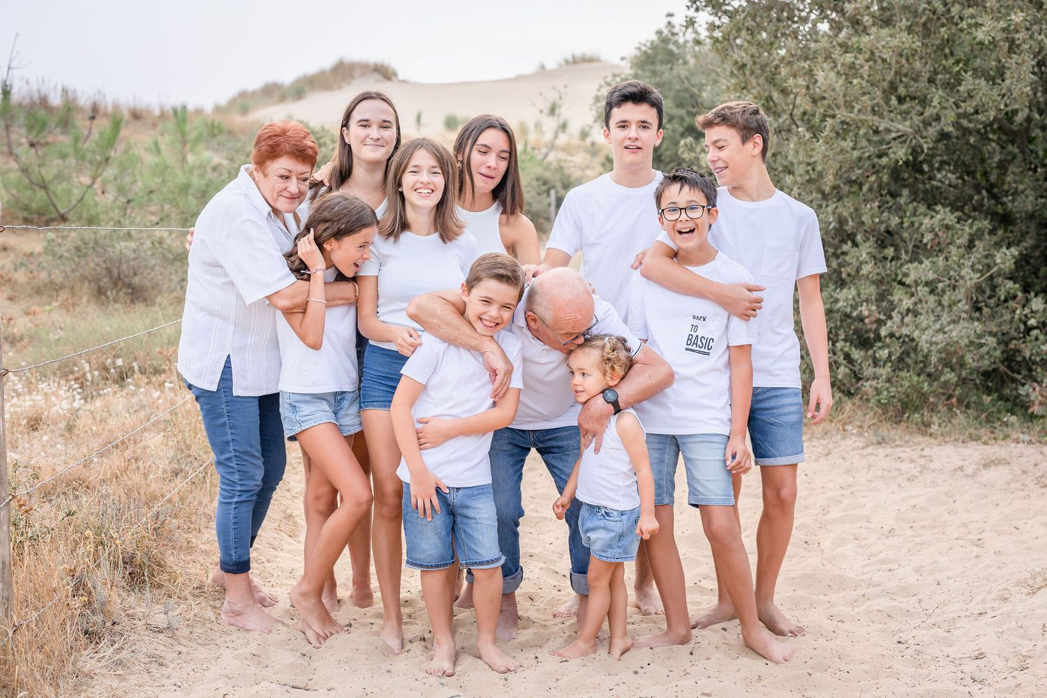 Multi-generational family in matching white and blue casual wear poses outdoors.