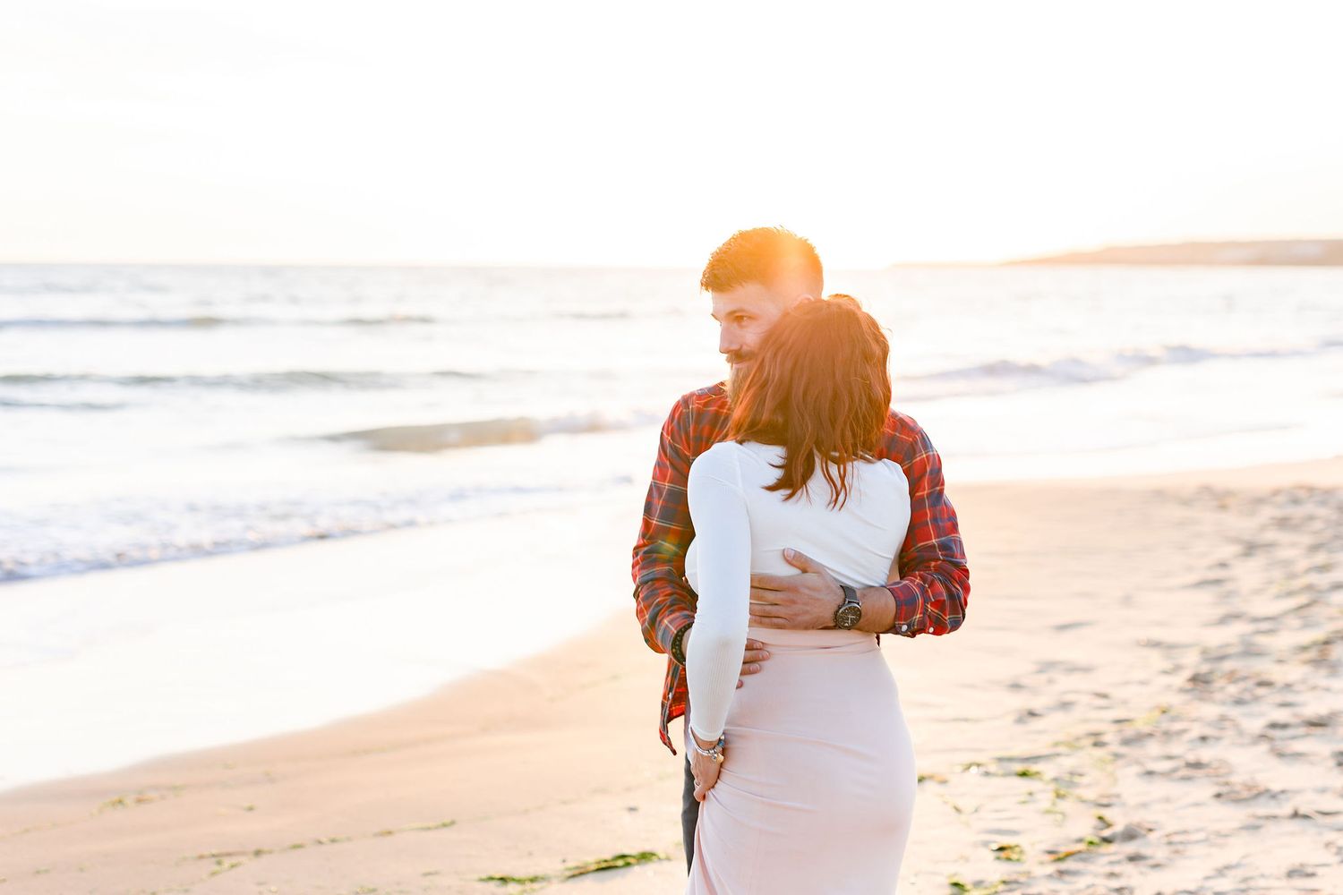 Beach maternity photoshoot silhouettes against ocean waves at sunset.