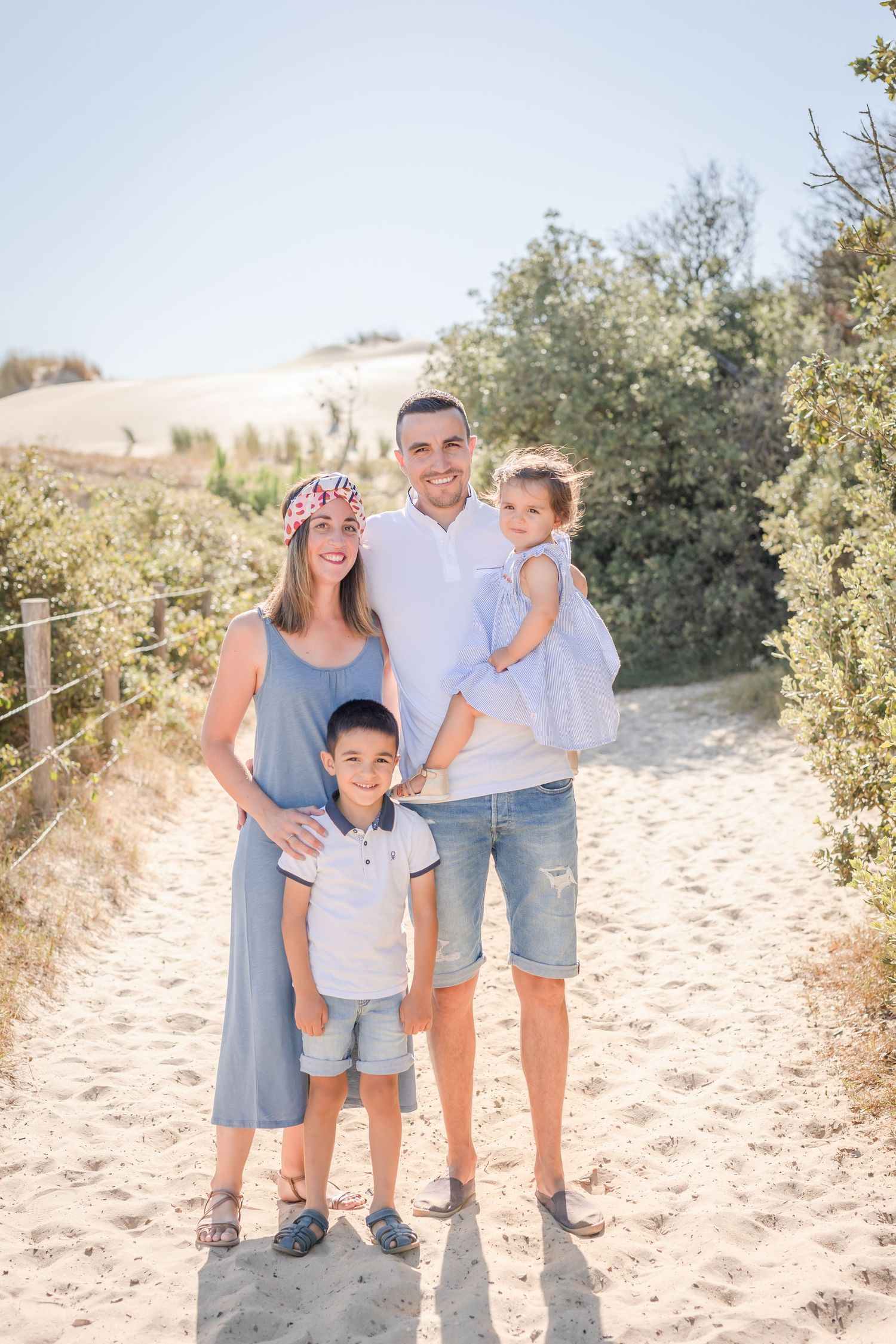 A family in coordinated blue and white outfits poses together on sandy beach dunes.