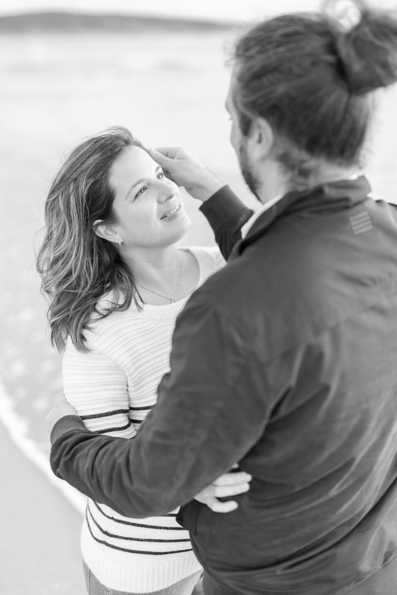 A couple shares an intimate moment on a beach in black and white photography.