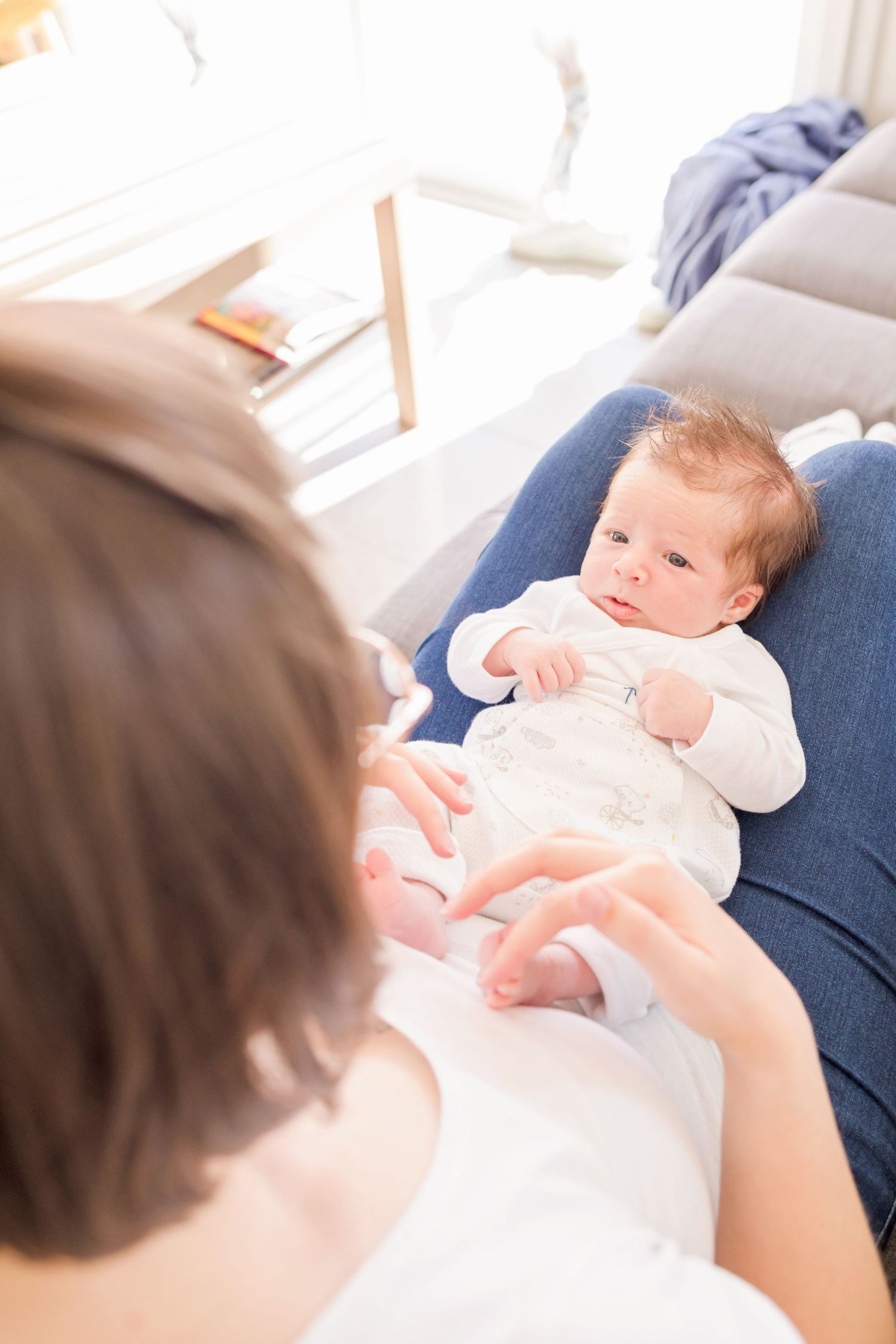 Baby in white onesie lying on blue cushion while being entertained.