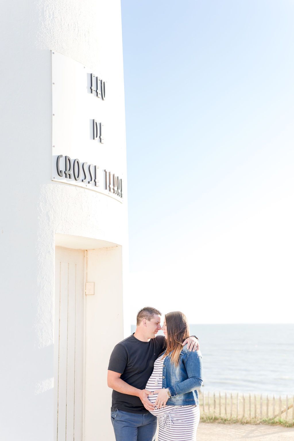 Couple sharing intimate moment by white lighthouse overlooking ocean.