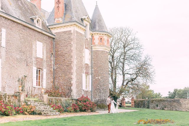 A romantic scene of a couple walking near a grand French chateau with stone walls and towers.