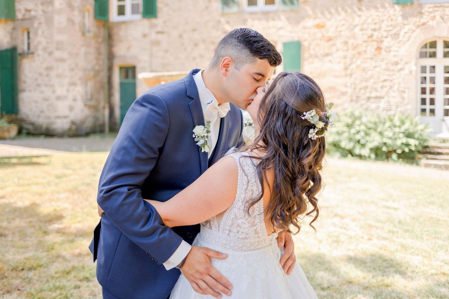 Newlyweds share intimate moment outside historic stone building with green shutters.