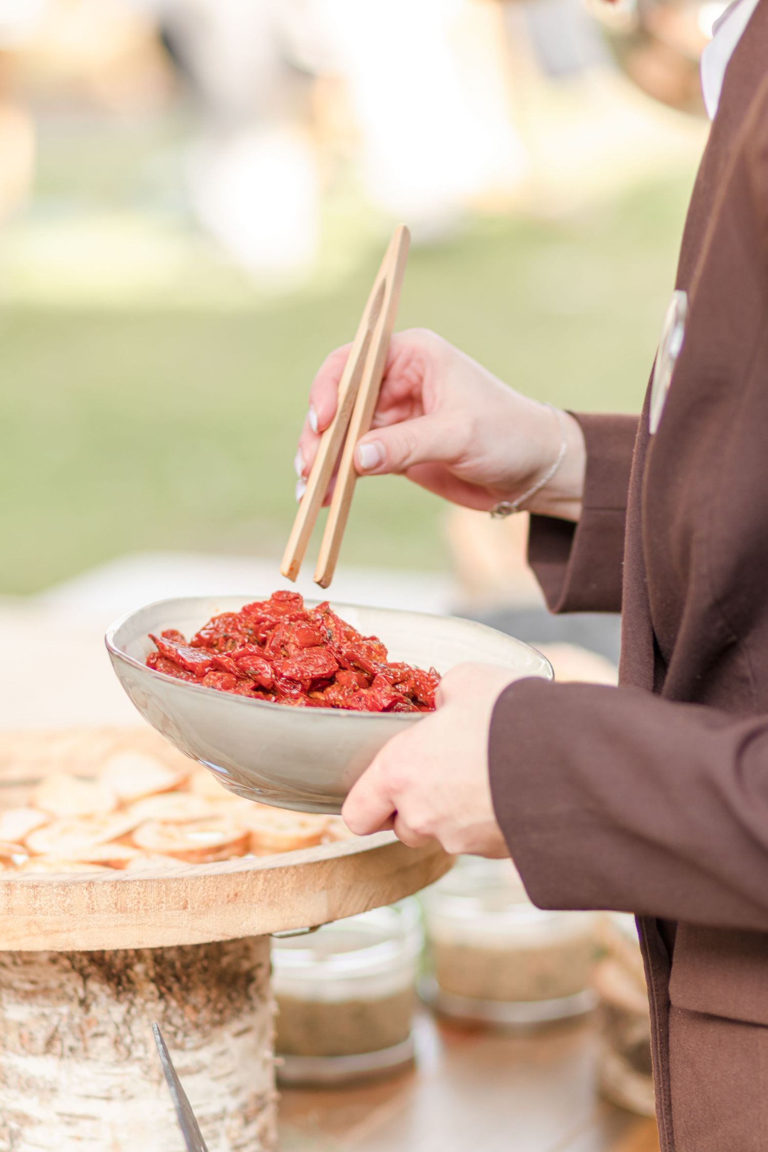 Server holding wooden platter with tuna tartare and chopsticks at catered event.