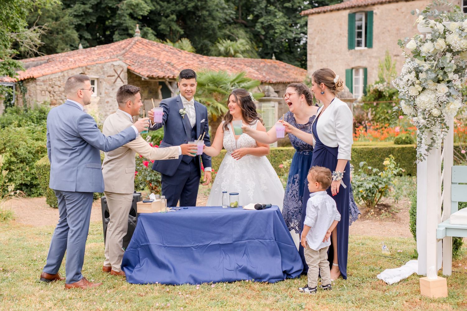 Wedding party gathered around a blue-clothed table performing a ceremony outdoors.