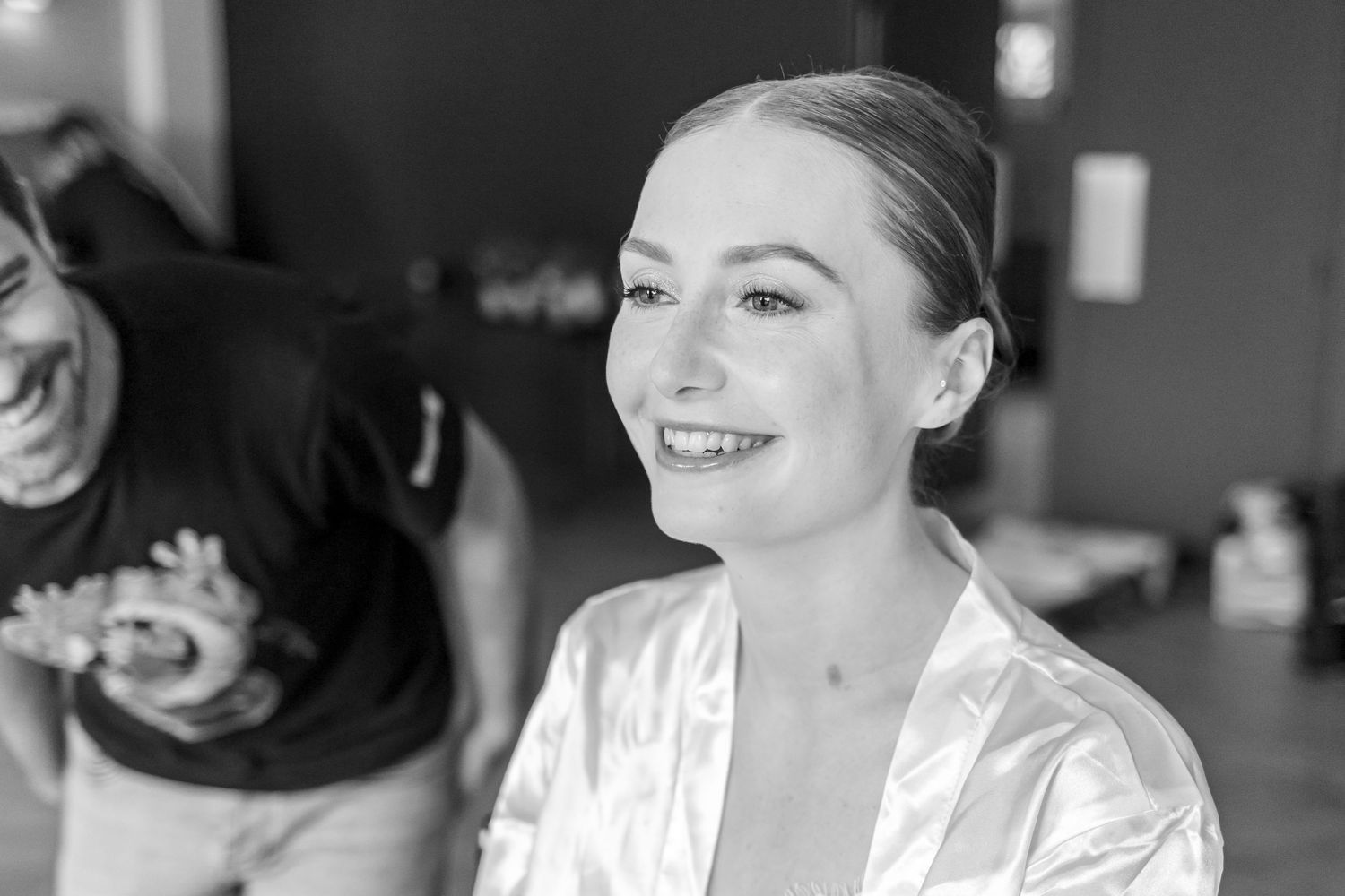 Black and white portrait of person in satin robe smiling during wedding preparations.