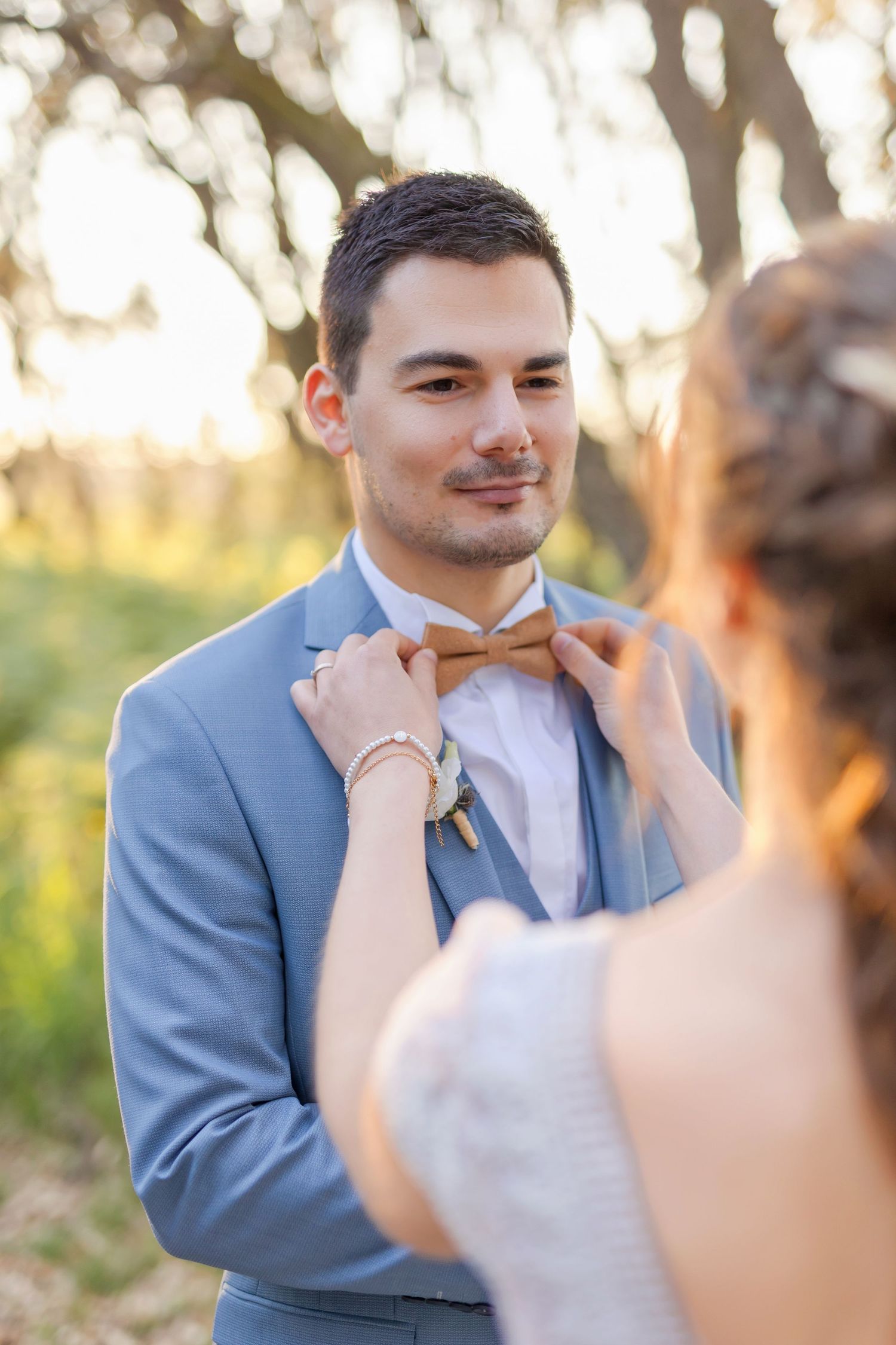 Close up shot of a light blue suit being adjusted with a peach colored bowtie at sunset.