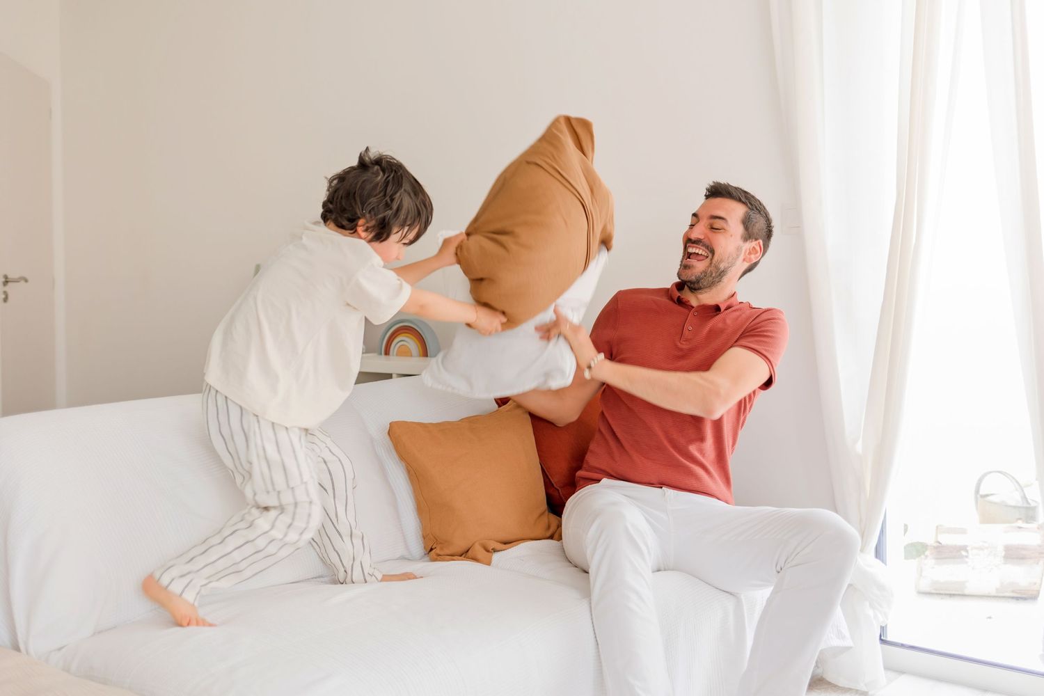 Joyful playtime with cushions on a white sofa in natural light.